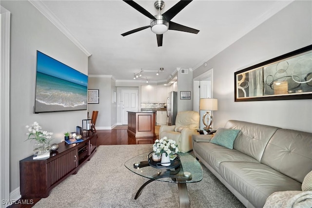 living room featuring wood finished floors, a ceiling fan, baseboards, ornamental molding, and rail lighting