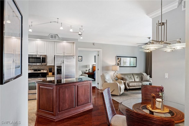 kitchen with dark countertops, appliances with stainless steel finishes, ornamental molding, open floor plan, and white cabinetry