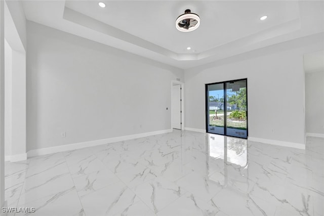 empty room with recessed lighting, a raised ceiling, marble finish floor, and baseboards