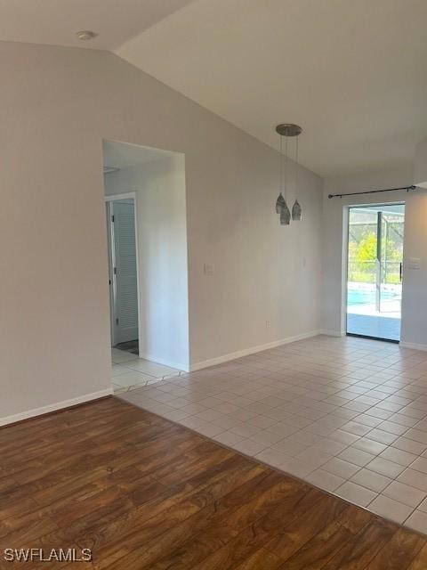 empty room with vaulted ceiling, light wood-style flooring, and baseboards