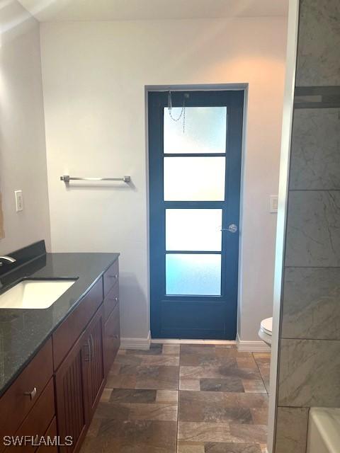 full bath featuring a bathing tub, vanity, toilet, and baseboards