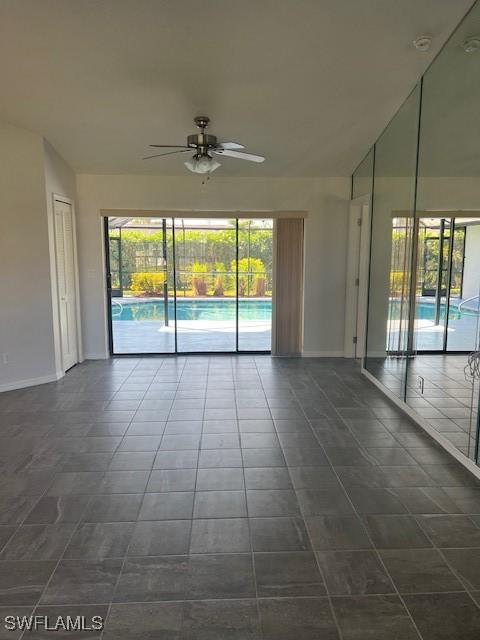 spare room with ceiling fan, dark tile patterned flooring, lofted ceiling, and baseboards