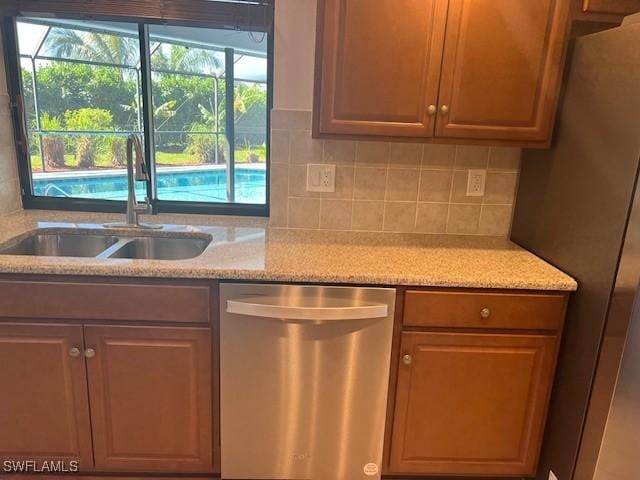 kitchen with stainless steel appliances, backsplash, a sink, and light stone countertops