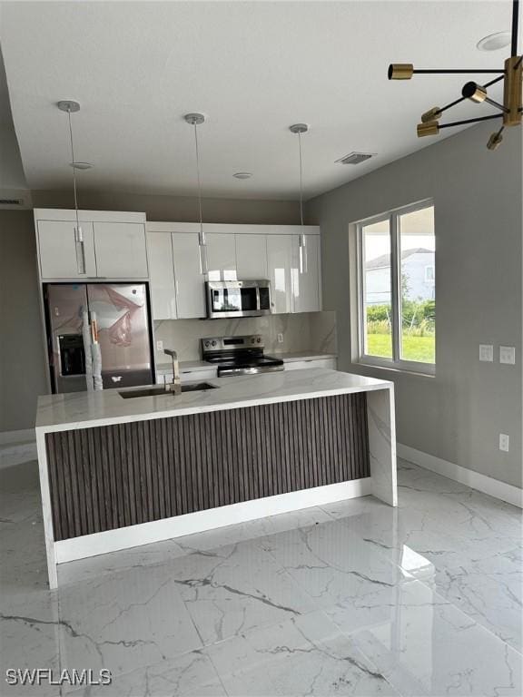 kitchen featuring sink, pendant lighting, stainless steel appliances, white cabinets, and a kitchen island with sink