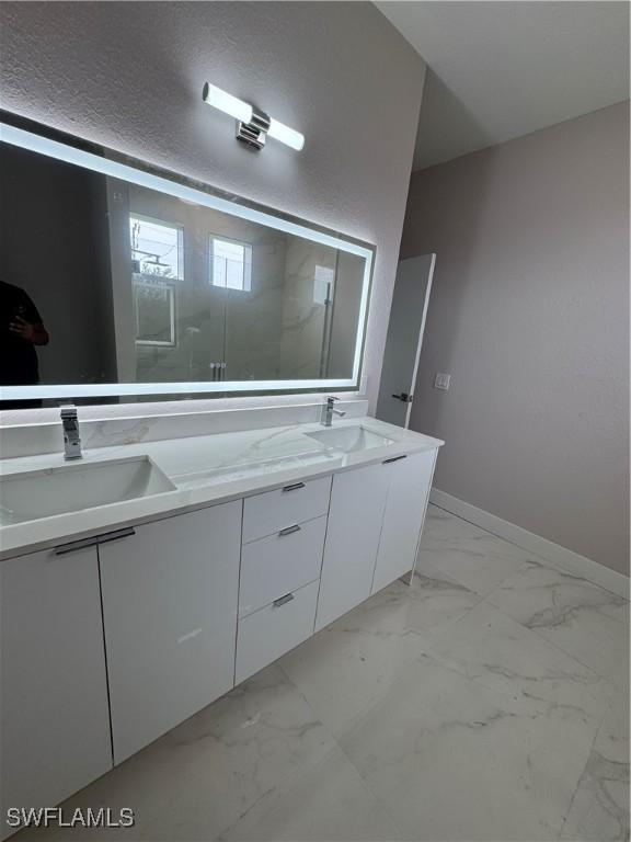 2810 27th St SW, Lehigh Acres, FL 33976 - full bathroom with double vanity, marble look tile flooring, baseboards, and a shower with shower door