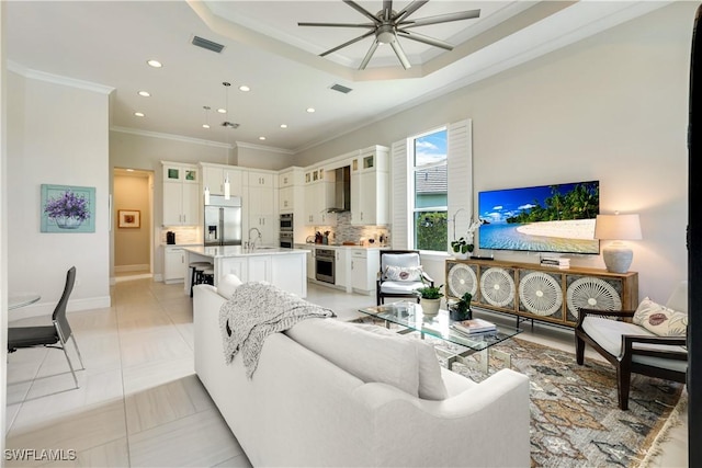 living room featuring a tray ceiling, recessed lighting, visible vents, and crown molding