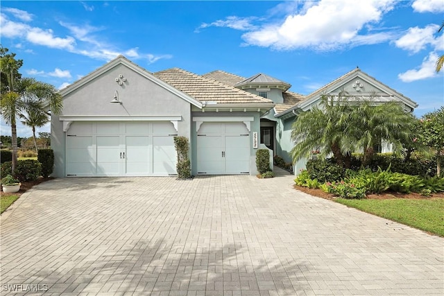 view of front facade featuring a garage, decorative driveway, a tiled roof, and stucco siding