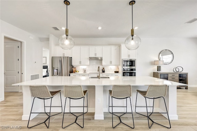 kitchen featuring sink, white cabinetry, decorative light fixtures, stainless steel fridge, and a large island