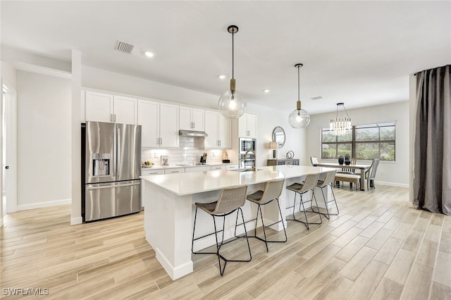 kitchen featuring sink, white cabinetry, a center island with sink, pendant lighting, and stainless steel appliances