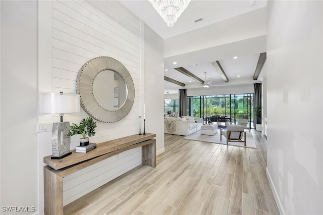 hall featuring beam ceiling, light hardwood / wood-style floors, and a chandelier