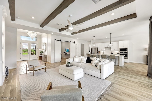 living room featuring beamed ceiling, ceiling fan, light hardwood / wood-style floors, a barn door, and french doors