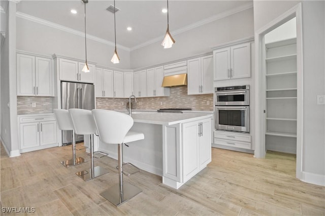 kitchen featuring appliances with stainless steel finishes, an island with sink, pendant lighting, and white cabinets