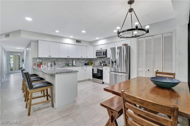 kitchen featuring stainless steel appliances, hanging light fixtures, a peninsula, and white cabinetry