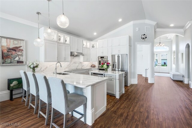 kitchen featuring arched walkways, appliances with stainless steel finishes, glass insert cabinets, a peninsula, and hanging light fixtures