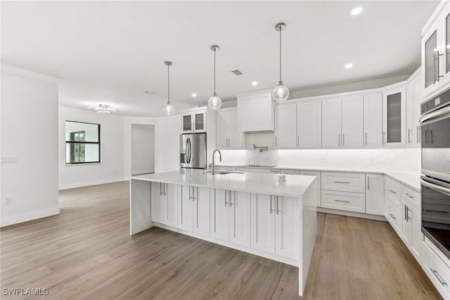 kitchen featuring appliances with stainless steel finishes, a kitchen island with sink, light countertops, and glass insert cabinets