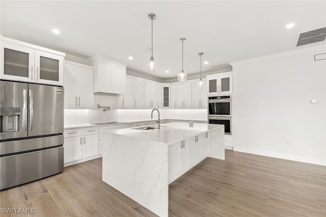 kitchen featuring glass insert cabinets, a kitchen island with sink, stainless steel appliances, white cabinetry, and a sink