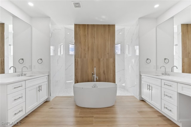 bathroom with a freestanding tub, visible vents, two vanities, and a sink