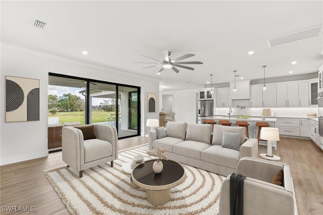 living area with visible vents, a ceiling fan, ornamental molding, light wood-type flooring, and recessed lighting