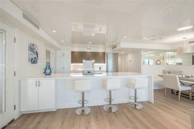 kitchen with a peninsula, a sink, a kitchen breakfast bar, light countertops, and light wood finished floors