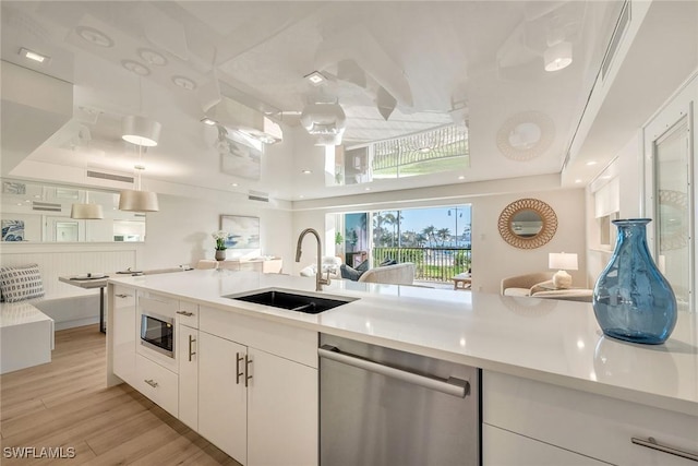 kitchen with stainless steel appliances, a sink, white cabinets, light countertops, and light wood-type flooring