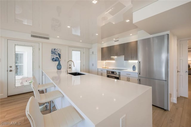 kitchen with a breakfast bar area, stainless steel appliances, light countertops, a sink, and light wood-type flooring