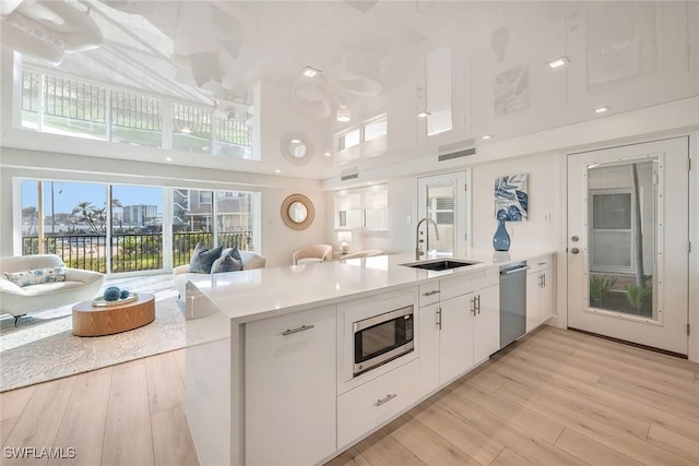 kitchen featuring light wood finished floors, white cabinets, stainless steel appliances, light countertops, and a sink