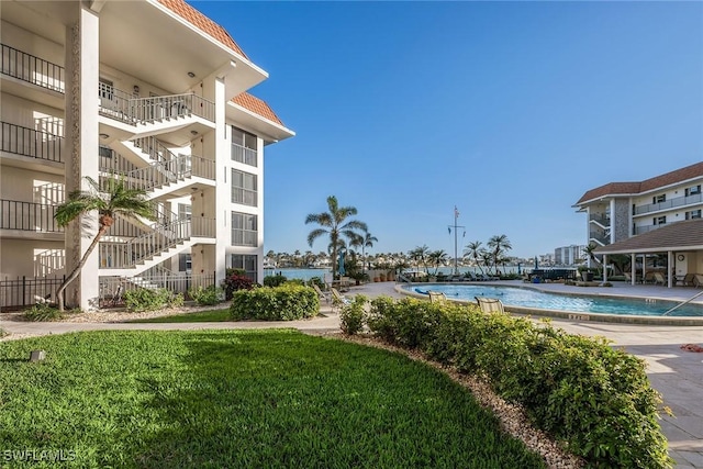 view of home's community with a swimming pool, a water view, and a lawn