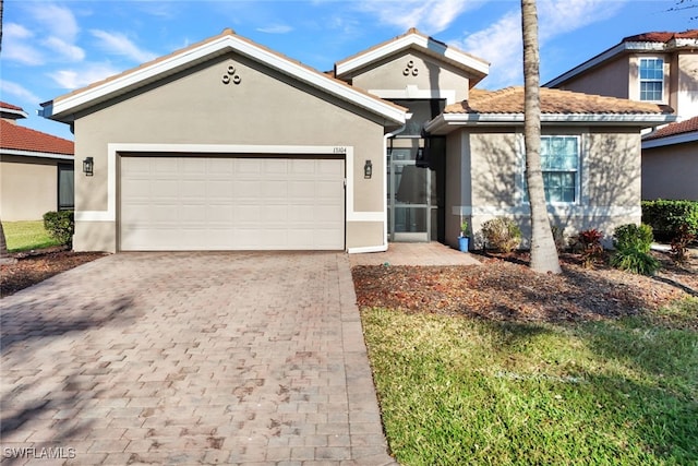 ranch-style home with decorative driveway, a tiled roof, an attached garage, and stucco siding