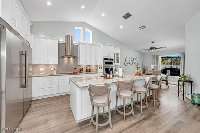 5548 Foxhunt Way, Naples, FL 34104 - kitchen with appliances with stainless steel finishes, wall chimney range hood, a kitchen island with sink, white cabinetry, and recessed lighting