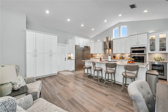 5548 Foxhunt Way, Naples, FL 34104 - kitchen featuring stainless steel appliances, beverage cooler, wall chimney exhaust hood, a breakfast bar area, and white cabinetry