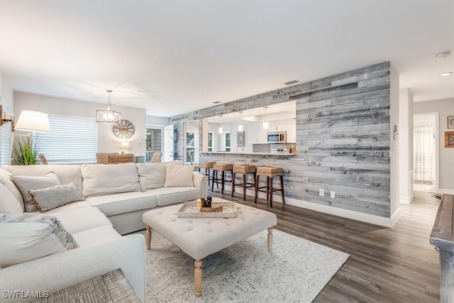 living area with an accent wall, wood finished floors, visible vents, and baseboards