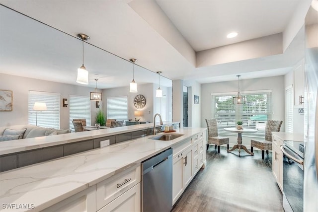 kitchen with light stone counters, stainless steel appliances, hanging light fixtures, white cabinetry, and a sink