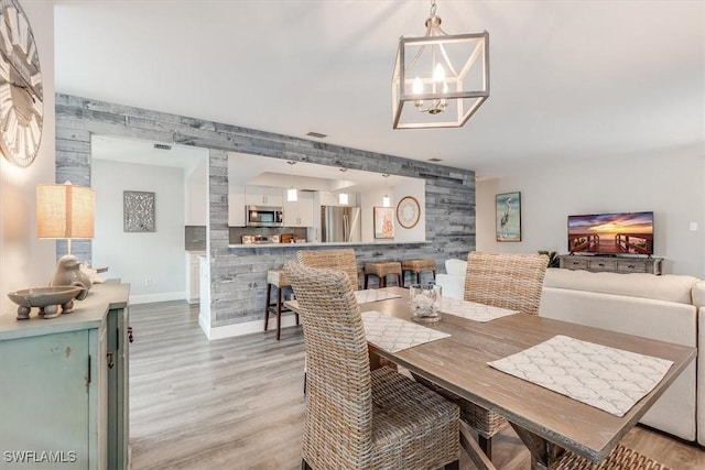 dining room with baseboards, an accent wall, a chandelier, and light wood-style floors