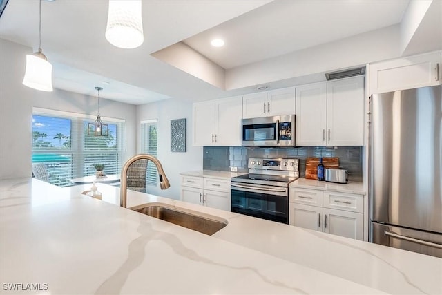 kitchen featuring appliances with stainless steel finishes, a sink, white cabinetry, and pendant lighting