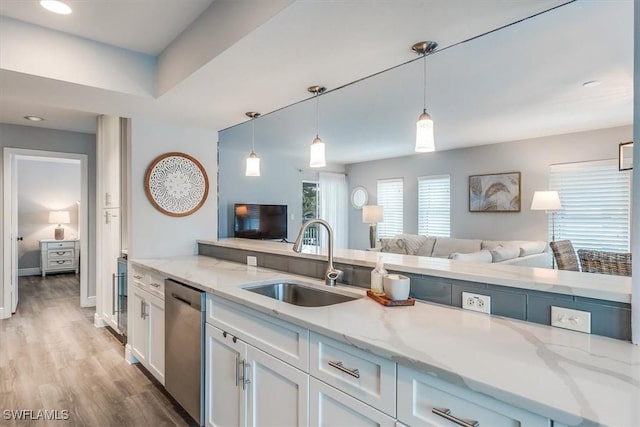 kitchen with light stone counters, open floor plan, white cabinetry, a sink, and dishwasher