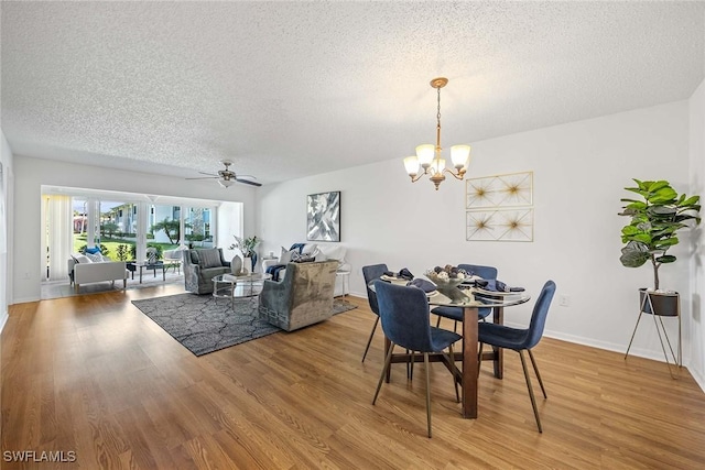 dining space featuring wood-type flooring, ceiling fan with notable chandelier, and a textured ceiling