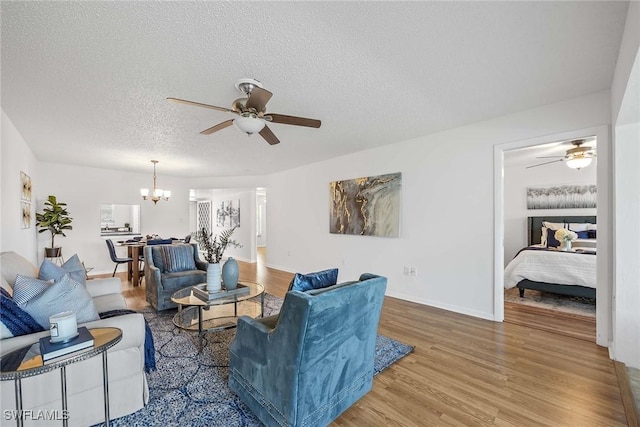 living room with hardwood / wood-style flooring, ceiling fan with notable chandelier, and a textured ceiling