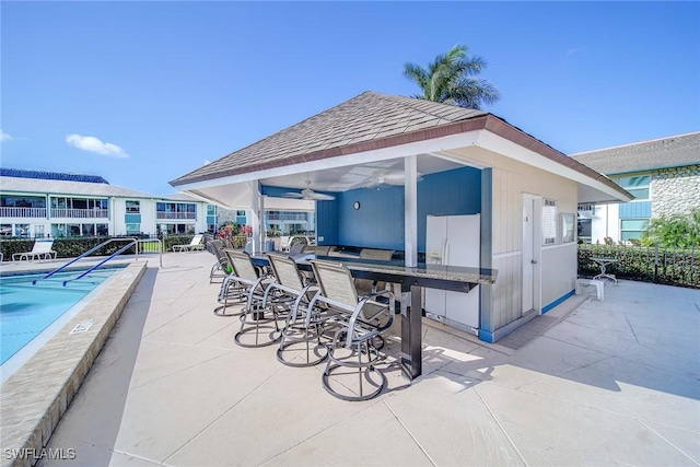 view of patio with a bar, ceiling fan, and a community pool