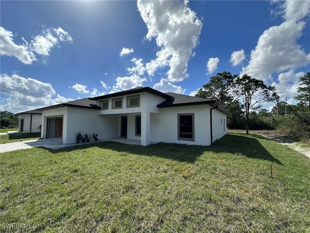 rear view of property featuring a garage, concrete driveway, a lawn, and stucco siding