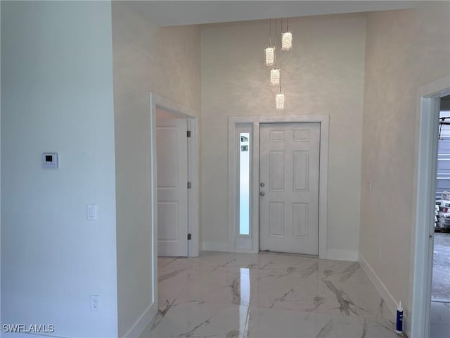 foyer entrance featuring marble finish floor, a high ceiling, and baseboards