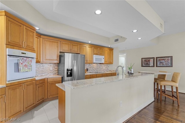 kitchen featuring decorative backsplash, white appliances, recessed lighting, a breakfast bar area, and a tray ceiling