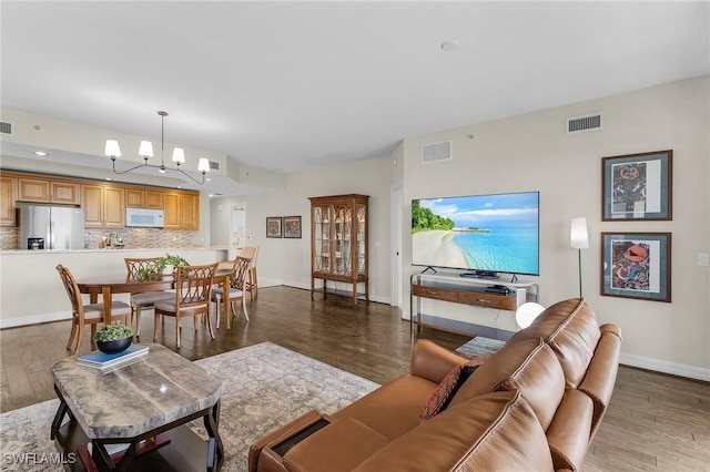 living area featuring baseboards, visible vents, a notable chandelier, and wood finished floors