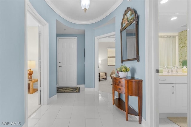hall featuring baseboards, crown molding, a sink, and light tile patterned floors