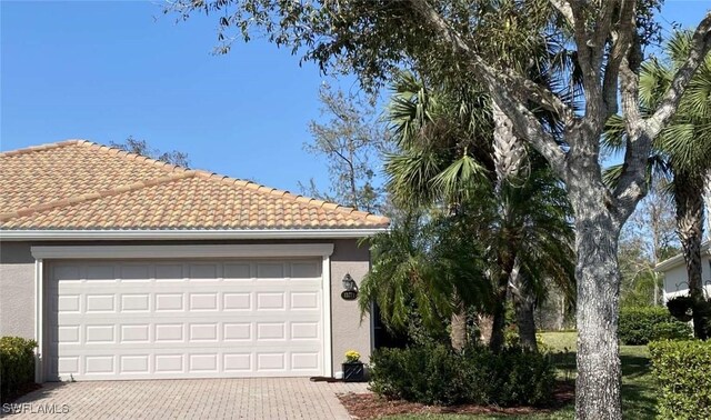 exterior space featuring decorative driveway, a tiled roof, an attached garage, and stucco siding