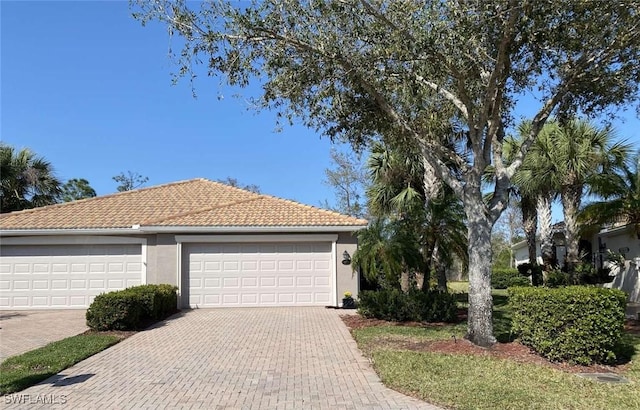 ranch-style home with a garage, a tile roof, and stucco siding