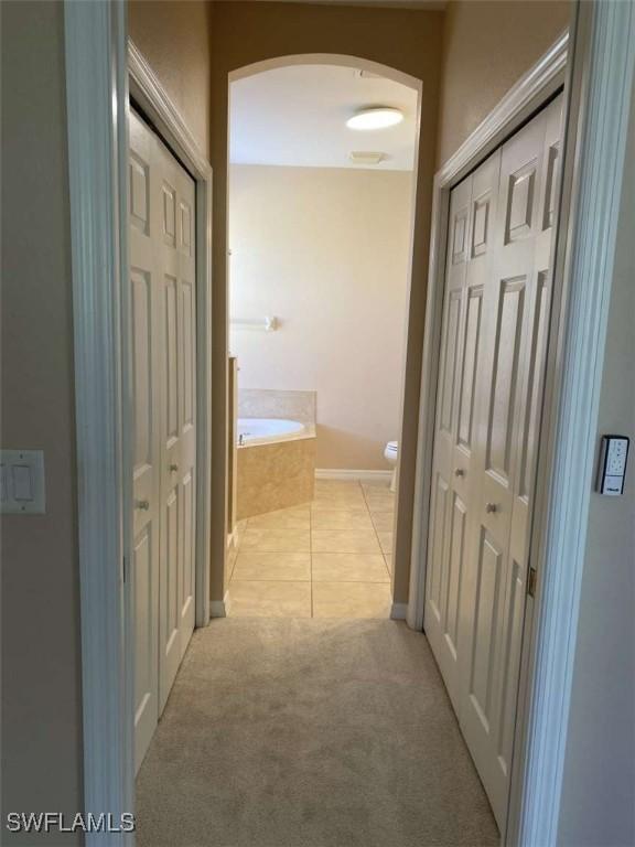 13772 Cleto Dr, Estero, FL 33928 - corridor featuring arched walkways, light tile patterned floors, light carpet, and baseboards