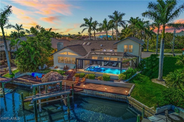 back of house featuring glass enclosure, an outdoor pool, boat lift, and a patio