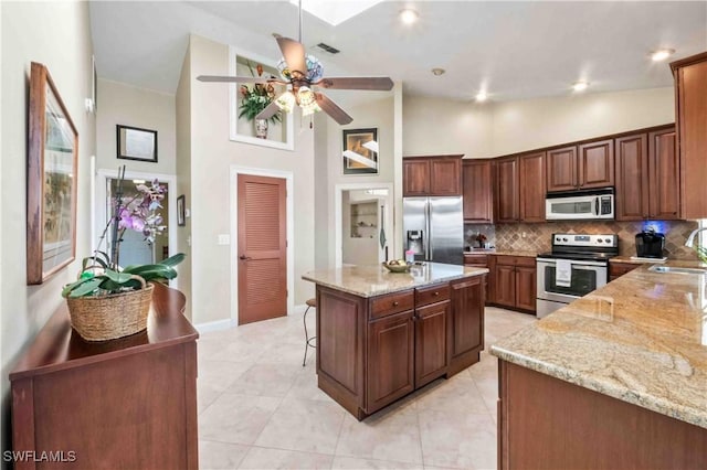 kitchen featuring stainless steel appliances, a kitchen island, a sink, and light stone countertops