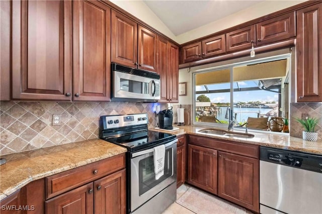 kitchen featuring light tile patterned floors, a sink, light stone countertops, stainless steel appliances, and backsplash