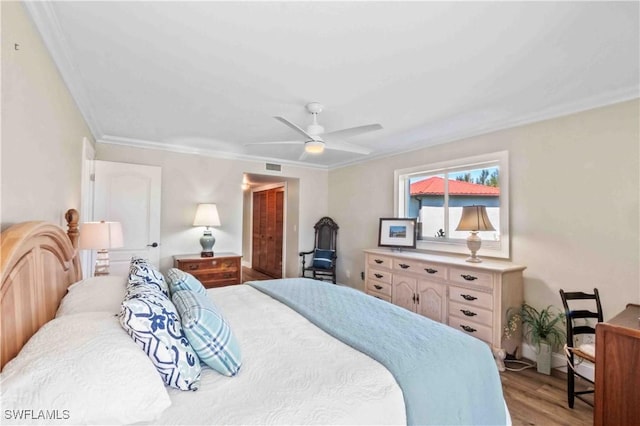 bedroom featuring a ceiling fan, visible vents, wood finished floors, and ornamental molding